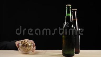 新鲜啤酒。 在木桌上用装有美味工艺啤酒的绿色和棕色小瓶旁的开心果碟递出去